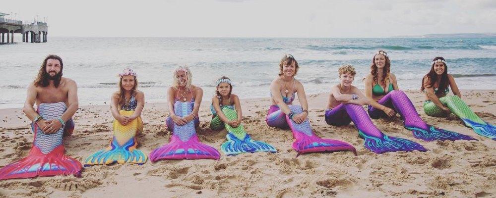 A group of people sat on a beach in front of the sea, dressed as mermaids
