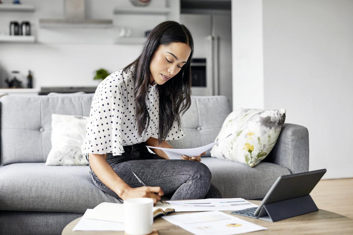woman writing looking at papers with a laptop on the table