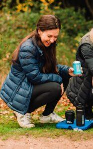 Rebecca Robinson - crouching and smiling whilst holding a can of lifted drinks