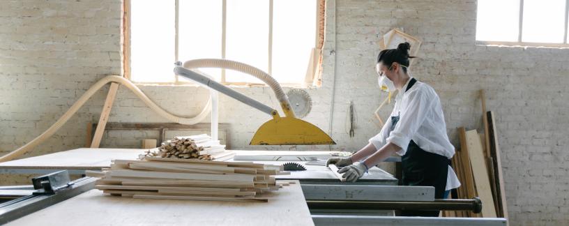 woman woodworking in workshop wearing safety gear and mask
