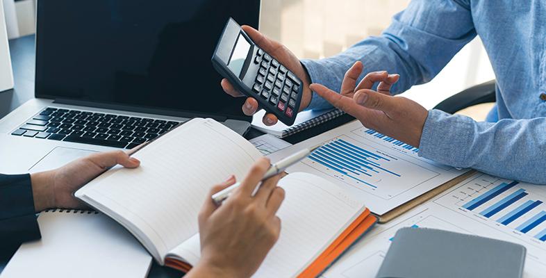 A close up shot two people, one with a calculator in their hands and the other with a notepad and pen