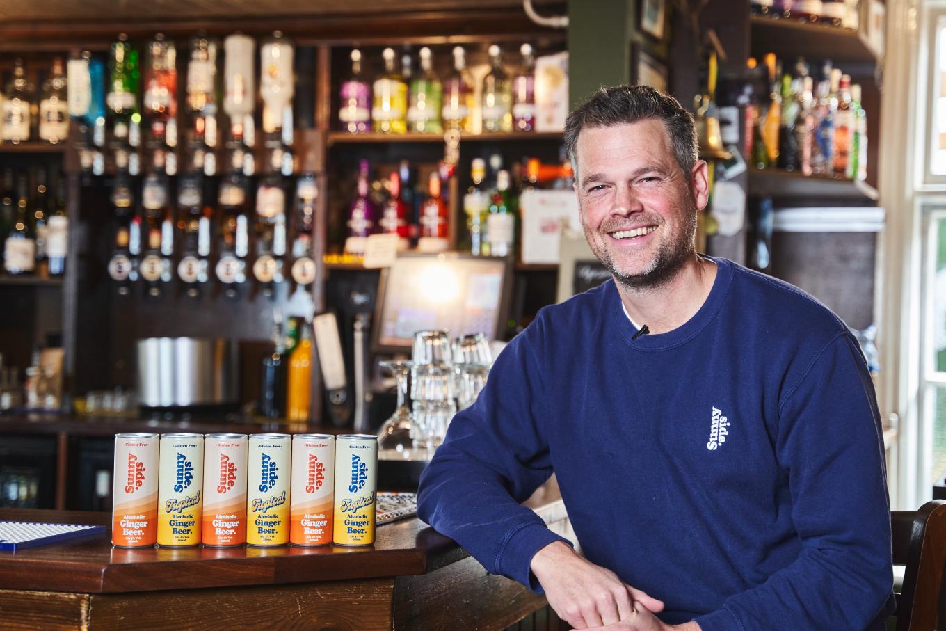 Founder of Sunny Side Drinks sat in a bar next to products