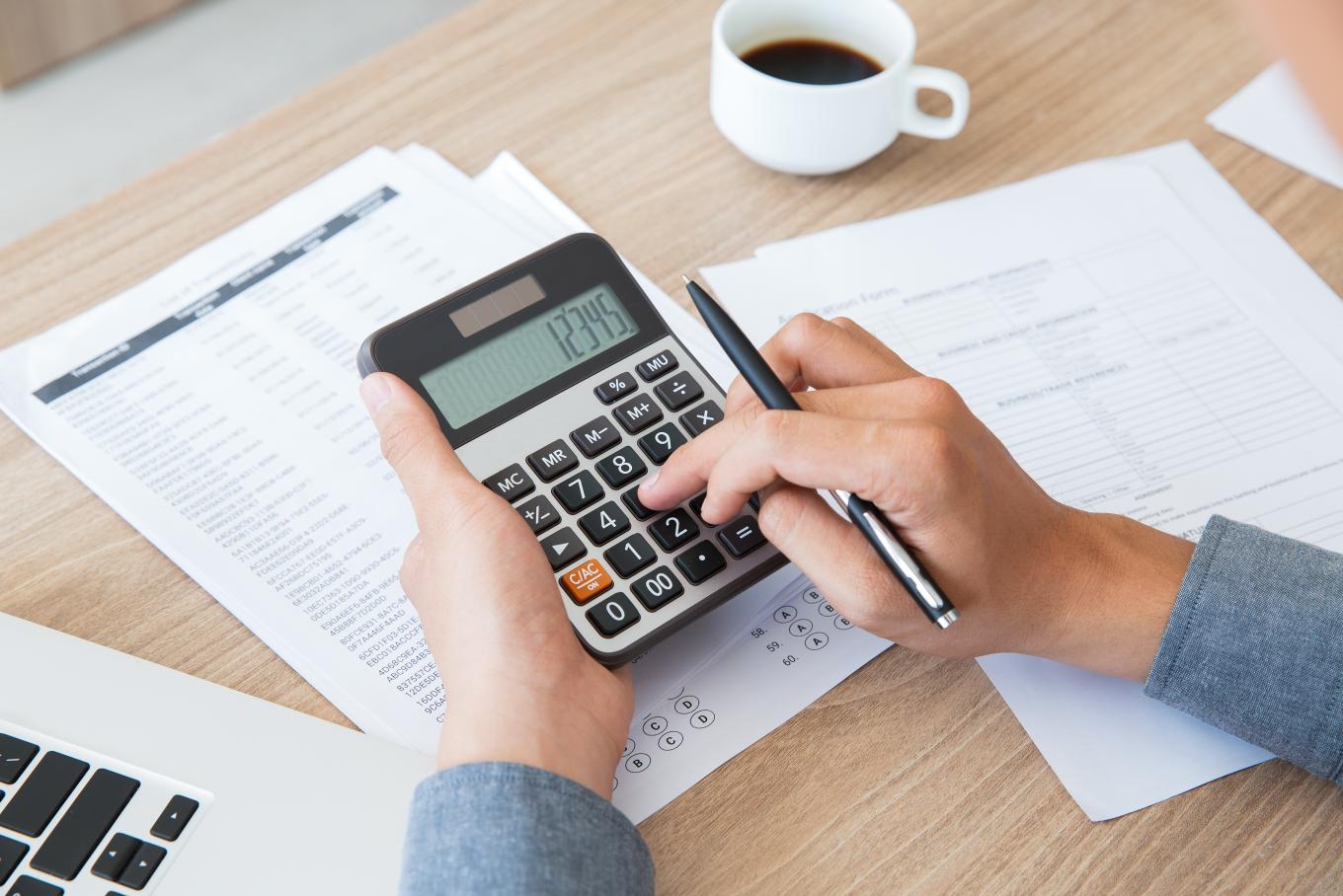 A view of a persons hands at a desk holding a calculator whilst doing paperwork