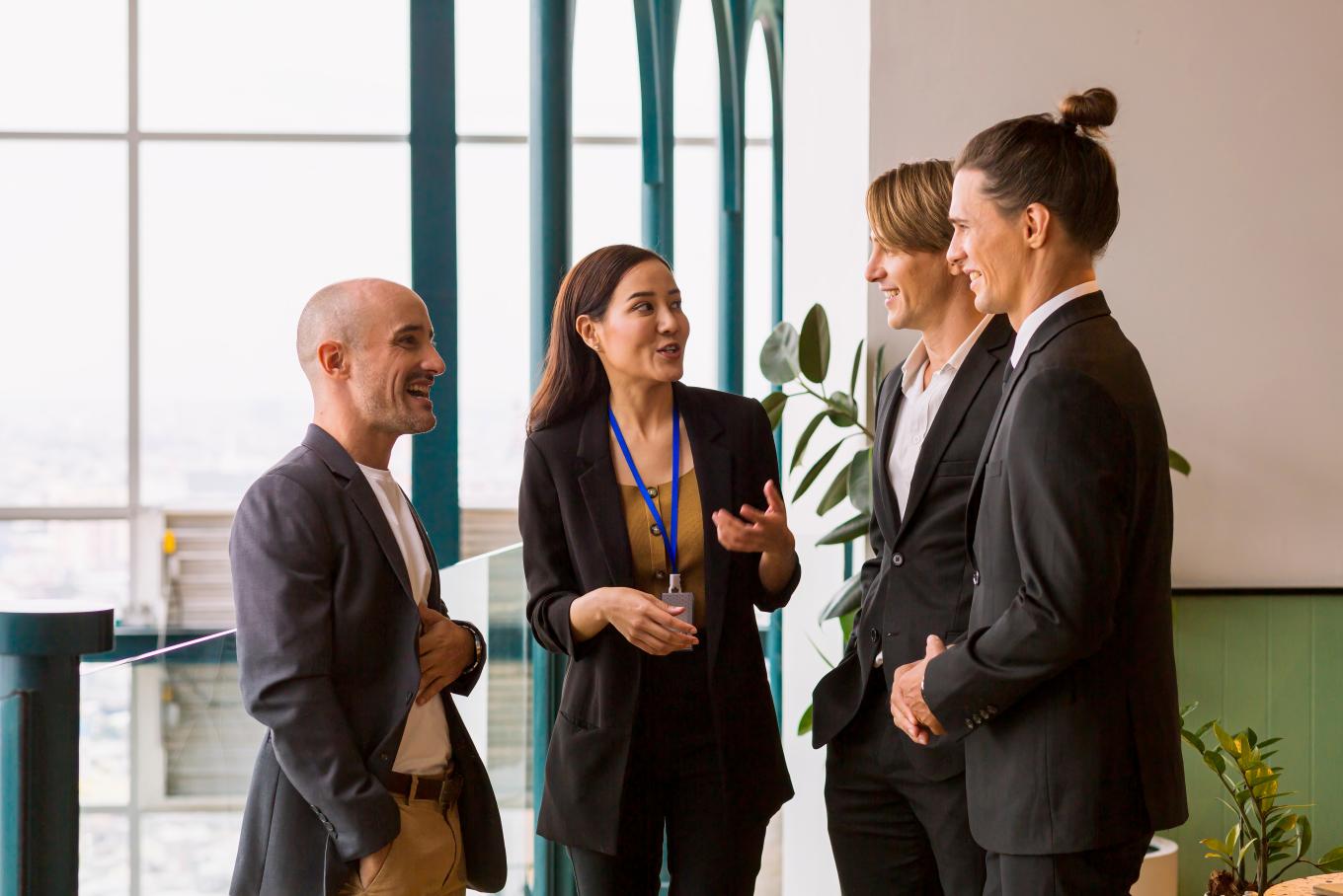 A group of four smartly dressed people, three male, one female in an informal conversation