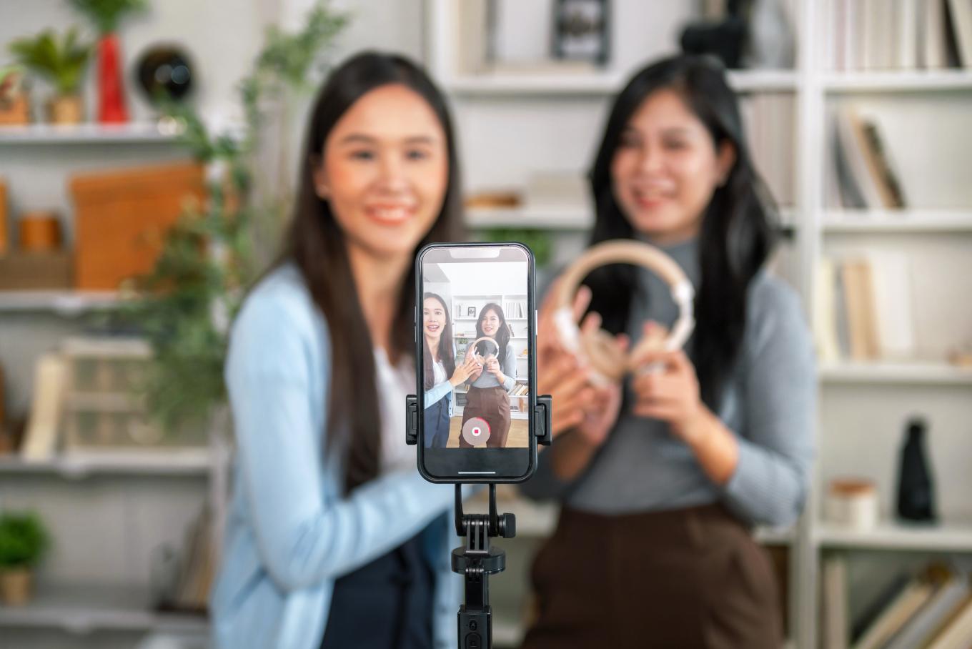 Two females standing behind a mobile device filiming themselves in selfie mode