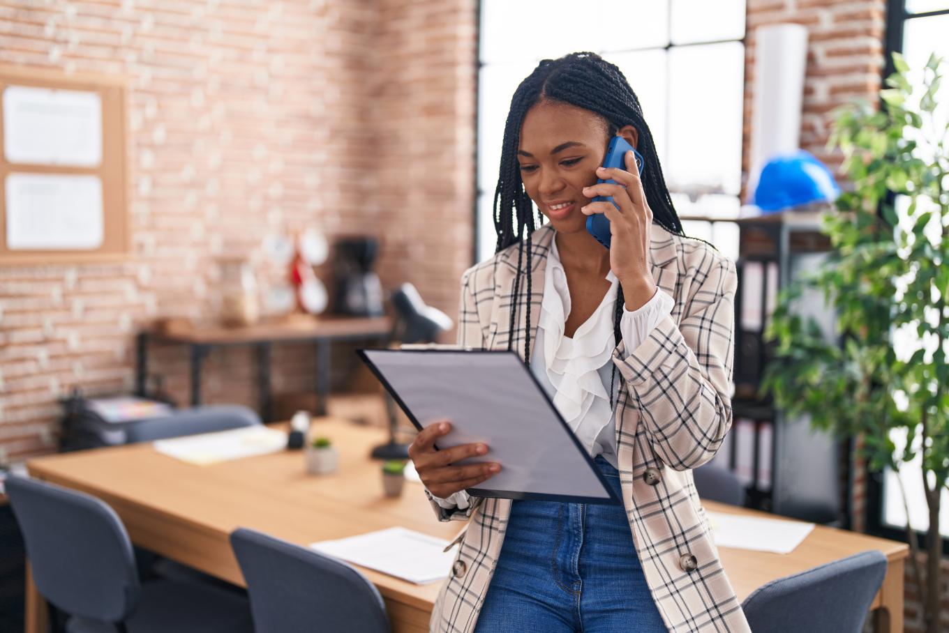Image of a lady, standing in an office environment holding a clipboard
