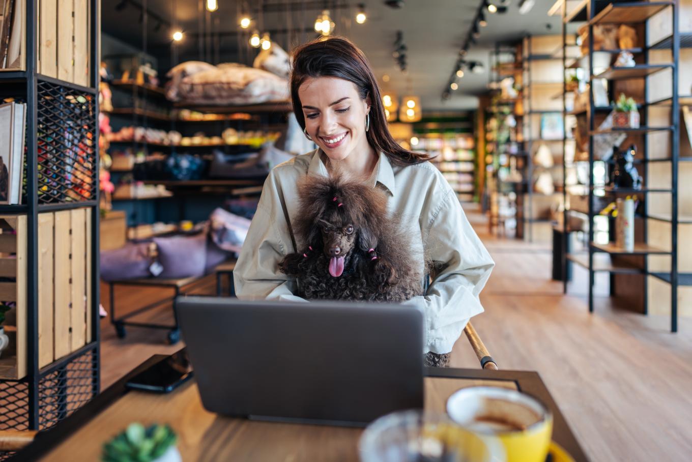 A female sat at a communal working space at a laptop with a dog sat on her lap