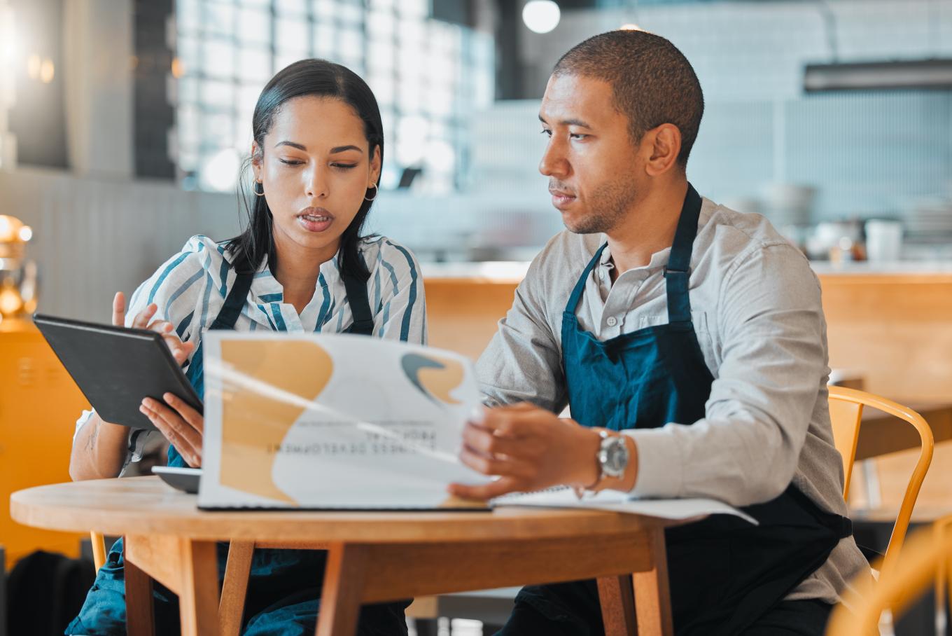 A male and female barista sat at a table in a cafe style environment